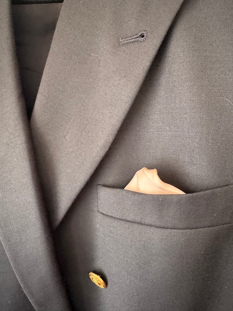Close-up of a dark gray textured blazer jacket with a single gold button and a beige pocket square in the breast pocket.