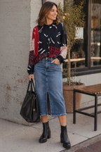 Woman wearing a colorful sweater, blue jeans, and black boots standing on a sidewalk.