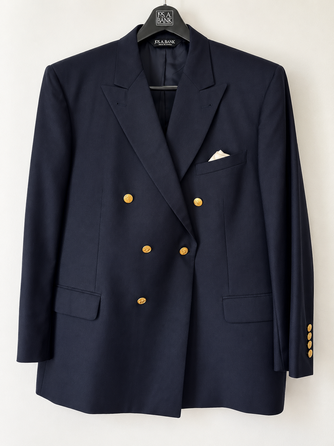A navy blue double-breasted blazer with gold buttons, hanging on a black hanger. It features notched lapels, flap pockets, and a white pocket square in the chest pocket.