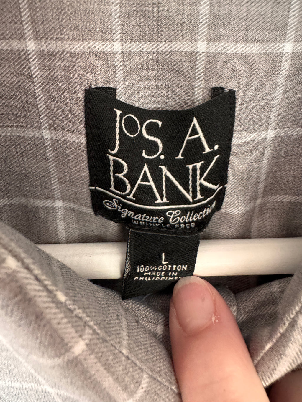 Close-up of a Jos. A. Bank clothing label sewn onto a gray plaid fabric garment, with a finger pointing at the label.