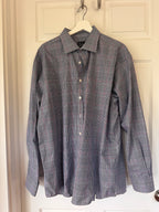 A long-sleeve plaid button-up shirt in blue, white, and red, hanging on a white hanger against a white paneled door.