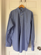 A blue long-sleeve button-down shirt with a subtle grid pattern, hanging on a wooden hanger against an off-white paneled door.