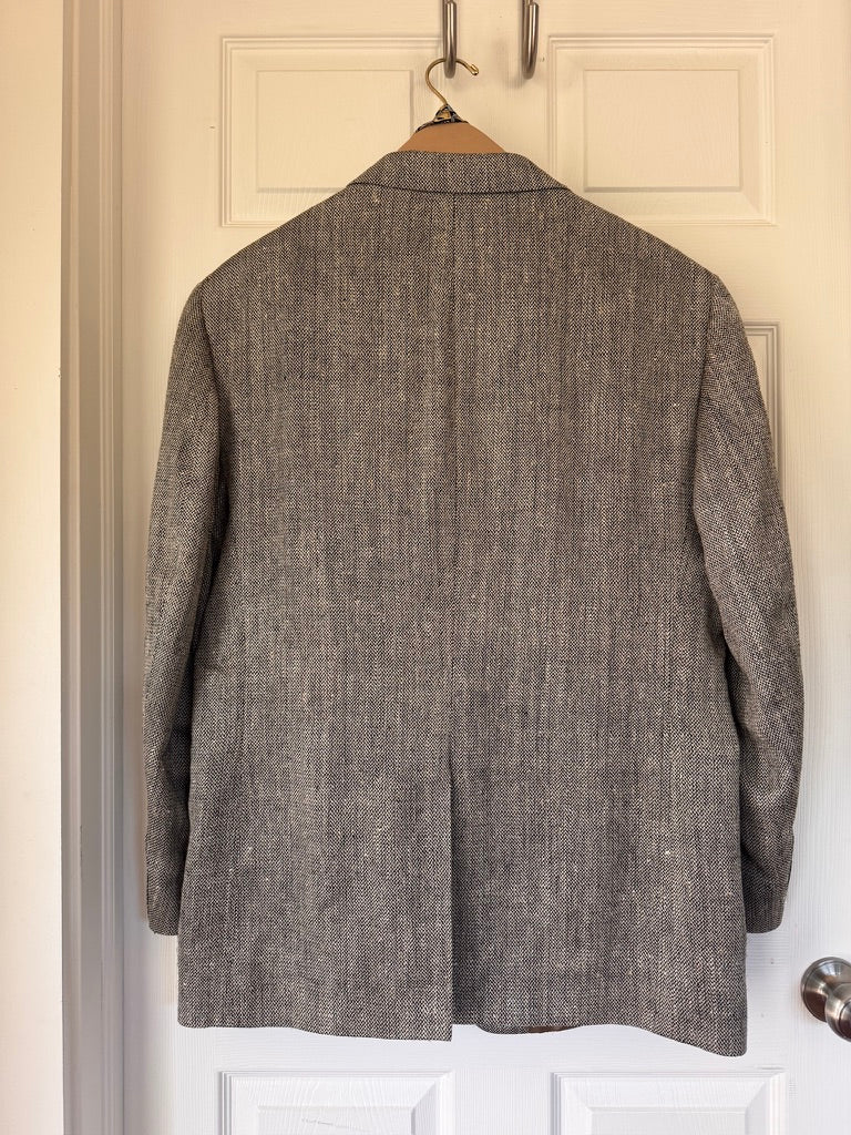 A textured gray wool blazer jacket hanging on a wooden hanger against a white paneled door.