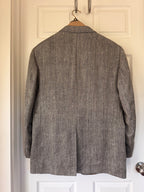 A textured gray wool blazer jacket hanging on a wooden hanger against a white paneled door.