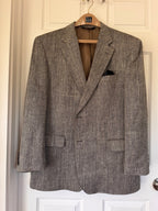 A textured black and brown tweed blazer jacket hanging on a wooden hanger against a white paneled door.