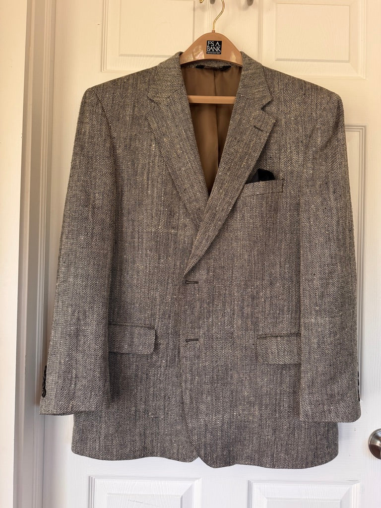 A textured black and brown tweed blazer jacket hanging on a wooden hanger against a white paneled door.