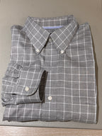 A folded gray plaid button-down shirt with white grid lines, laid flat on a textured beige surface.
