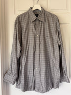 A gray and white plaid long-sleeve button-down shirt hanging on a white hanger against a white paneled door.
