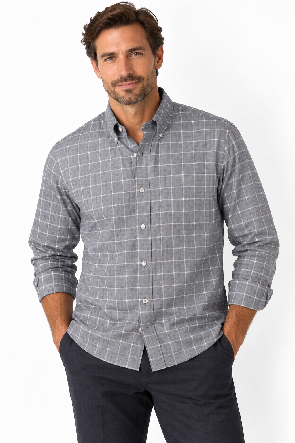 A man wearing a gray and white windowpane plaid long-sleeve button-down shirt, paired with dark navy pants, standing against a plain white studio background.