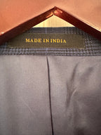 Close-up of the inner neck area of a garment, showing a dark gray textured inner collar band with a central label that reads 'MADE IN INDIA' in gold lettering. The garment fabric is a dark gray with a vertical center seam, and a brown hanger is visible at the top.