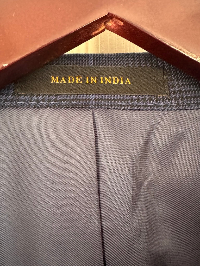 Close-up of the inner neck area of a garment, showing a dark gray textured inner collar band with a central label that reads 'MADE IN INDIA' in gold lettering. The garment fabric is a dark gray with a vertical center seam, and a brown hanger is visible at the top.