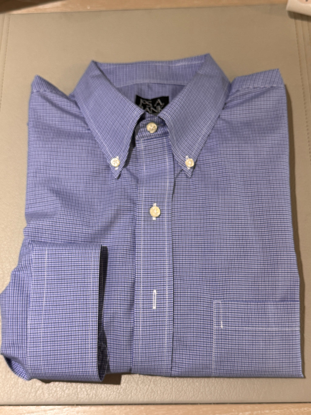 A folded blue and white checkered button-down shirt with a pointed collar and gold-tone buttons, laid flat on a beige surface.
