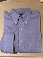 A folded blue and white checkered button-down shirt with a pointed collar and gold-tone buttons, laid flat on a beige surface.