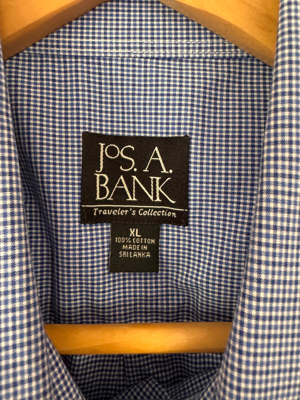 Close-up of the inside collar of a blue and white gingham shirt on a wooden hanger, showing the Jos. A. Bank brand label.