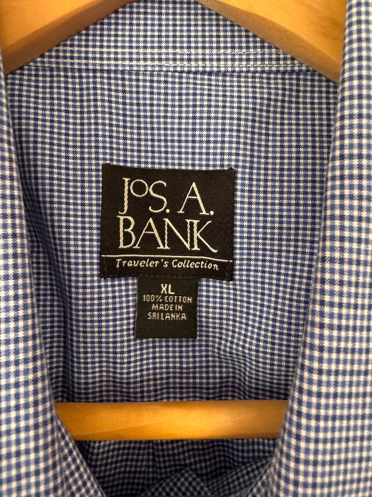 Close-up of the inside collar of a blue and white gingham shirt on a wooden hanger, showing the Jos. A. Bank brand label.