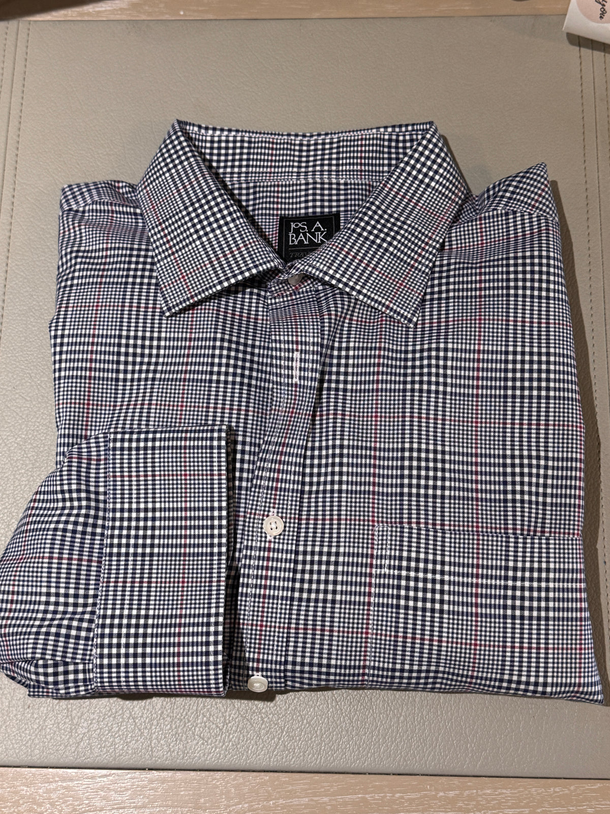 A folded long-sleeve button-up dress shirt with a small-scale blue, white, and red gingham pattern, displayed on a textured beige surface.
