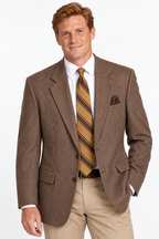A man wearing a brown houndstooth blazer, white dress shirt, a gold and brown striped tie, and khaki trousers, standing against a plain white background.
