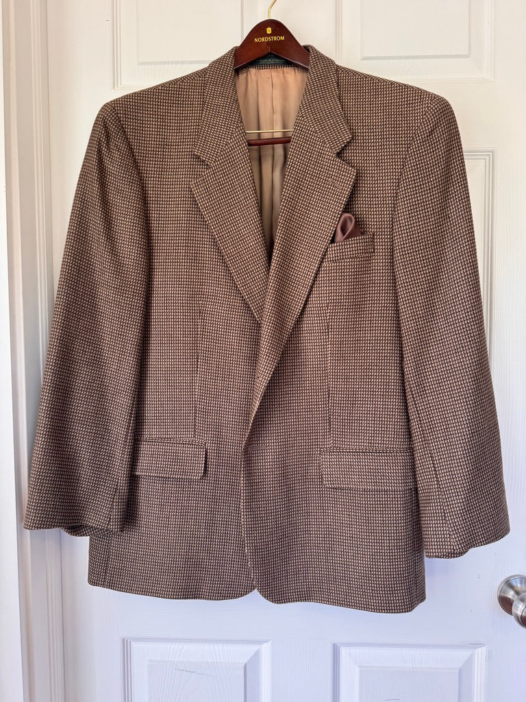 A brown and beige houndstooth patterned blazer jacket hanging on a wooden hanger against a white paneled door.