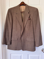 A brown and beige houndstooth patterned blazer jacket hanging on a wooden hanger against a white paneled door.