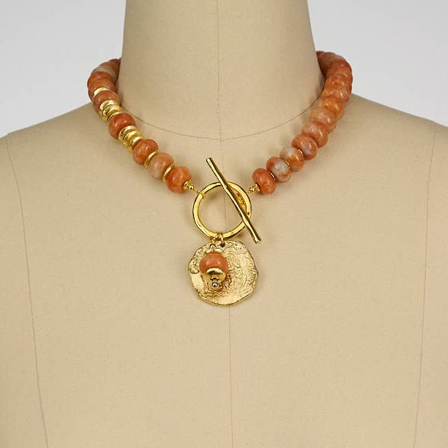 Necklace with orange beads and gold clasp on a mannequin bust against a white background