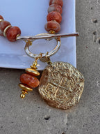 Necklace with gold and red beads on a textured surface