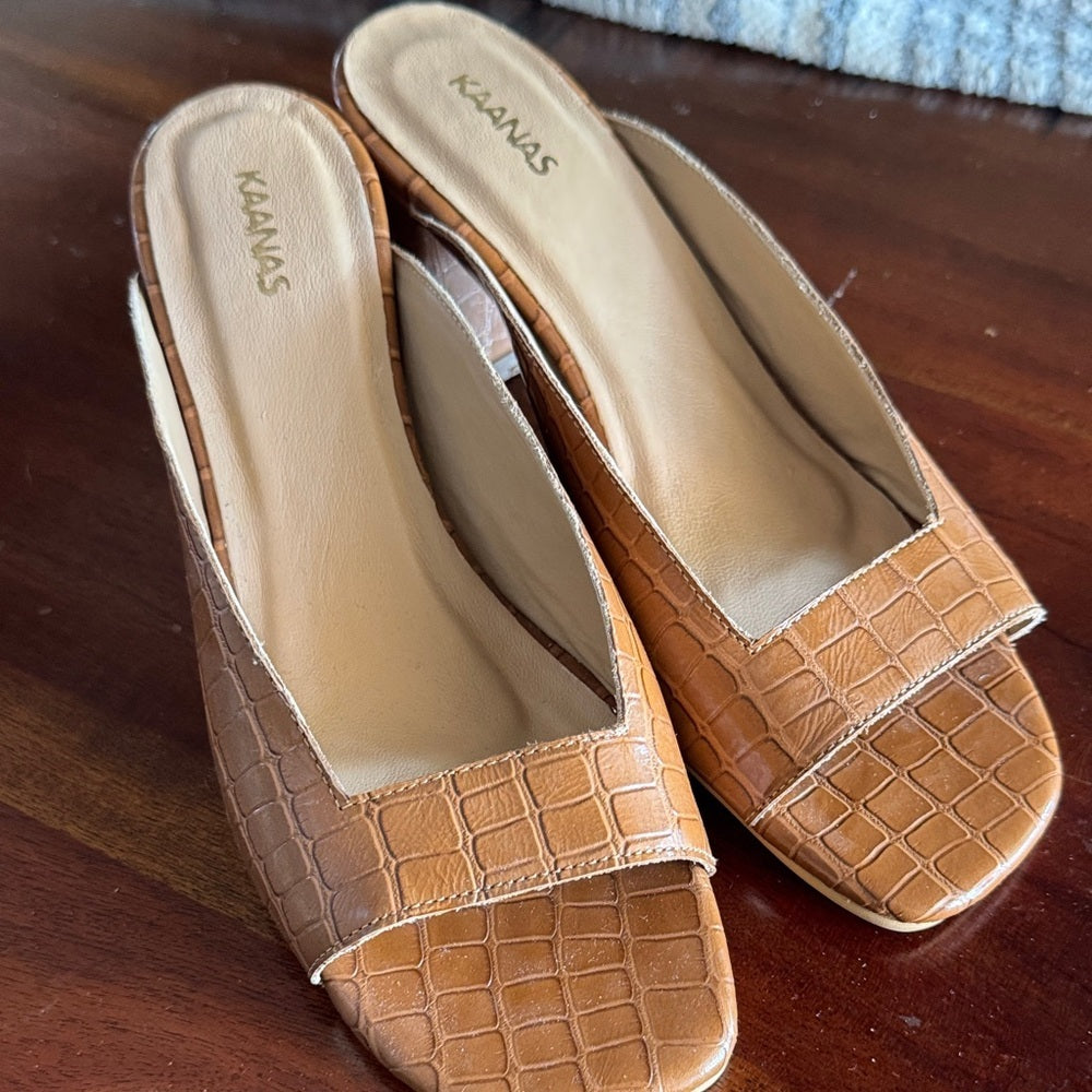 Pair of tan mules with textured design on a wooden surface