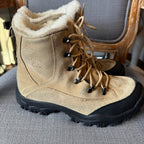 Pair of brown winter boots with black soles on a gray surface.
