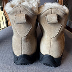 Pair of beige boots with black soles on a textured surface