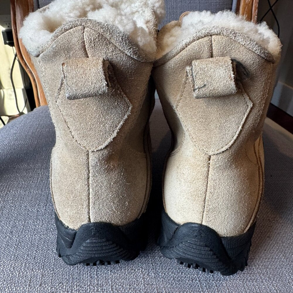 Pair of beige boots with black soles on a textured surface