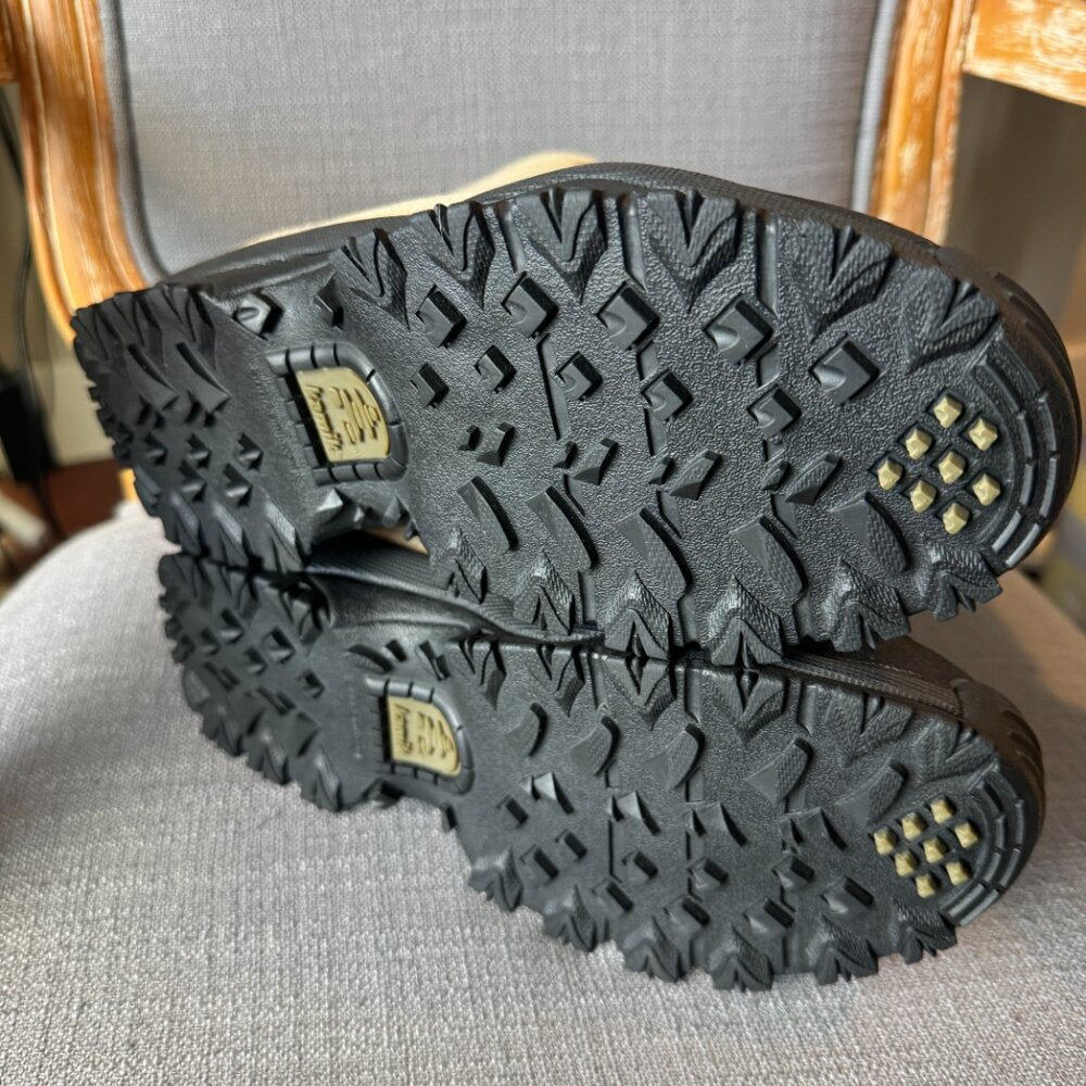 Close-up of black rubber boots with tread pattern on a gray surface