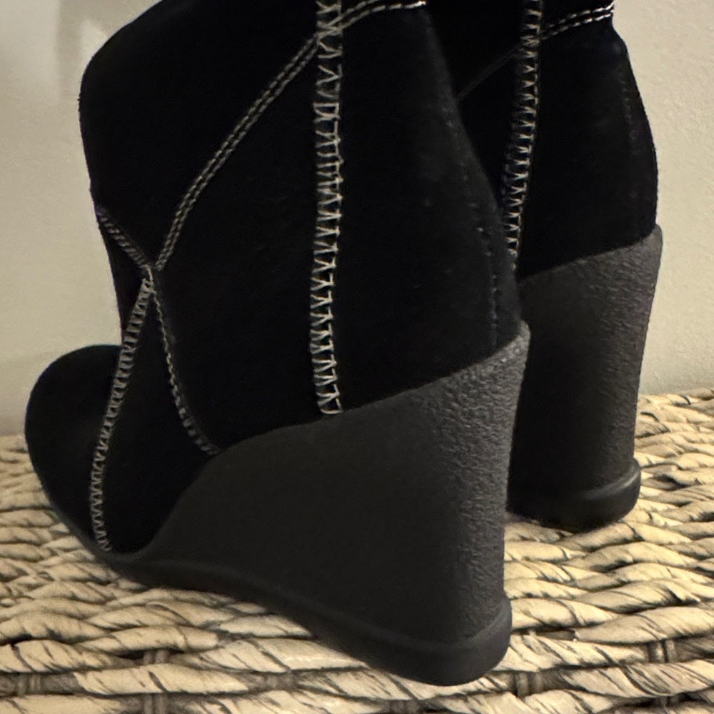Black wedge sandals with white stitching on a textured surface