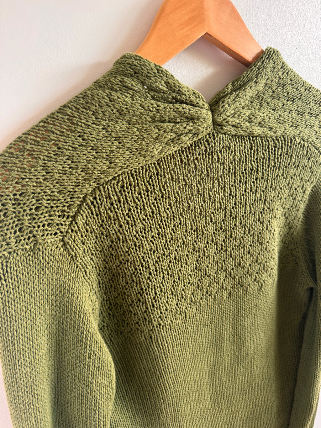 Close-up of a green knitted sweater on a wooden hanger against a white background