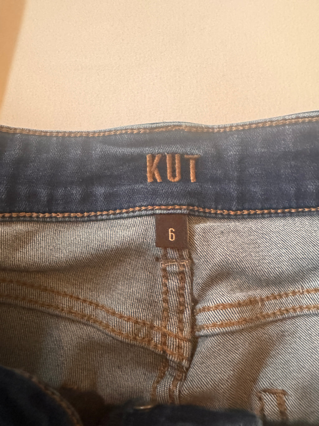 Close-up of denim fabric with 'KUT' branding on a beige background