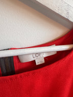 Close-up of a red garment with a white label inside, on a textured surface.