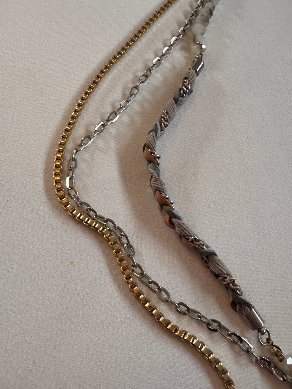 Three gold, silver, and bronze chain necklaces on a light gray background