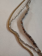 Three gold, silver, and bronze chain necklaces on a light gray background