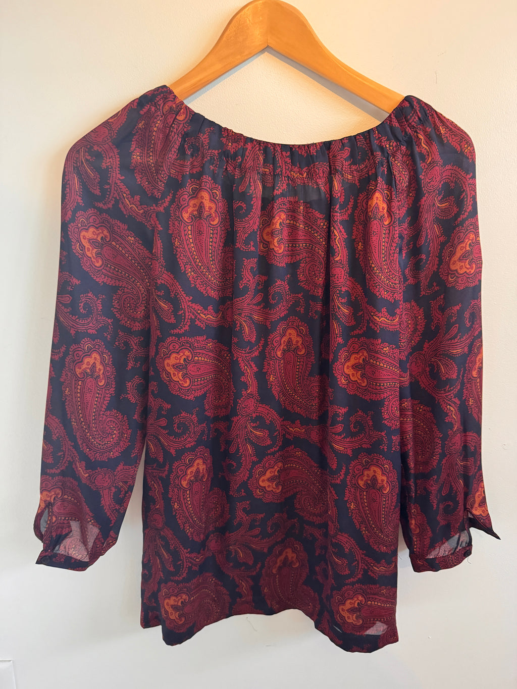 Red and black paisley patterned garment on a beige hanger against a white background
