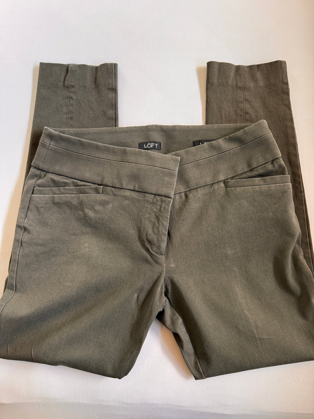 Folded olive green pants with a brand label on a white background