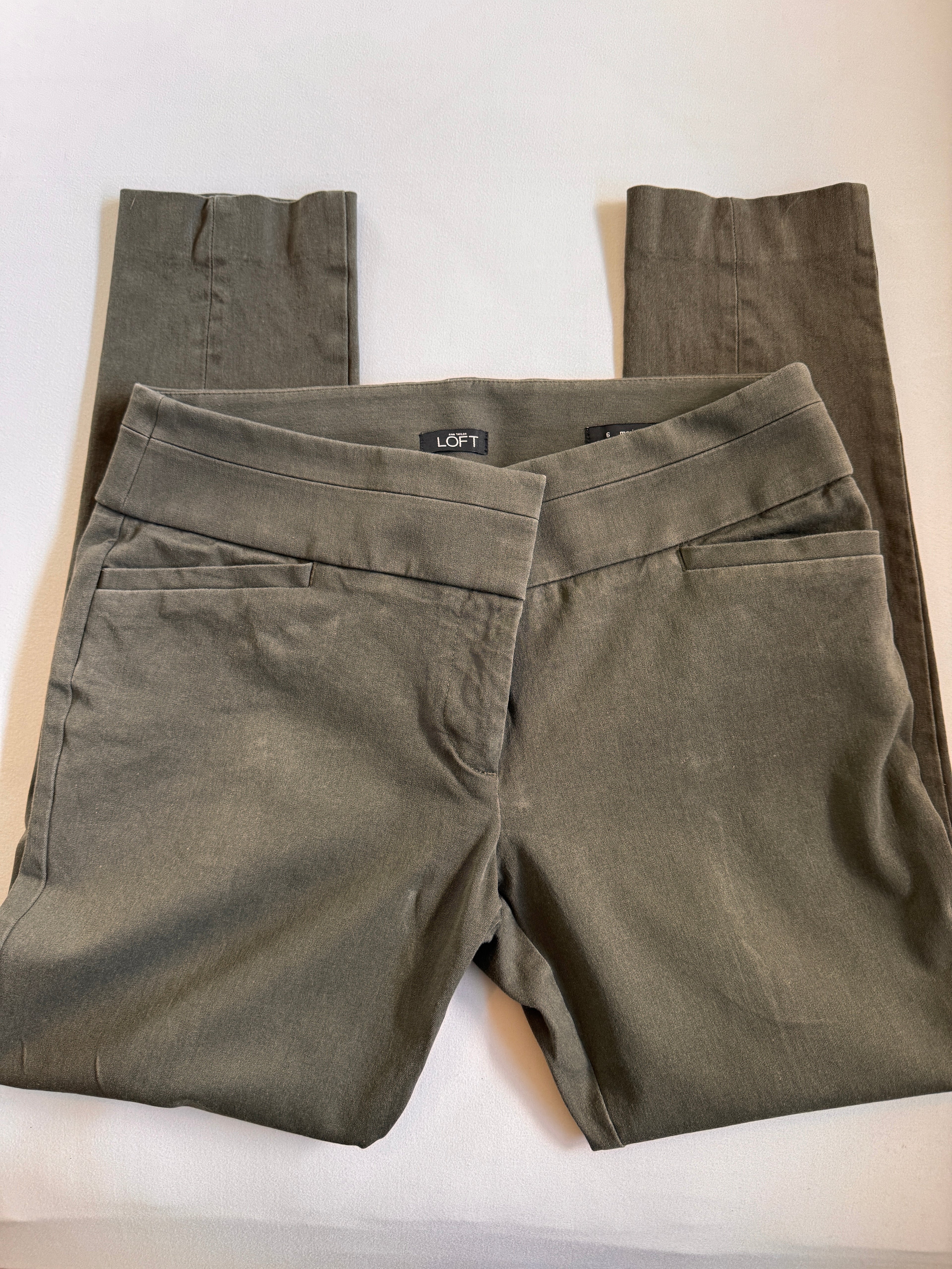 Folded olive green pants with a brand label on a white background