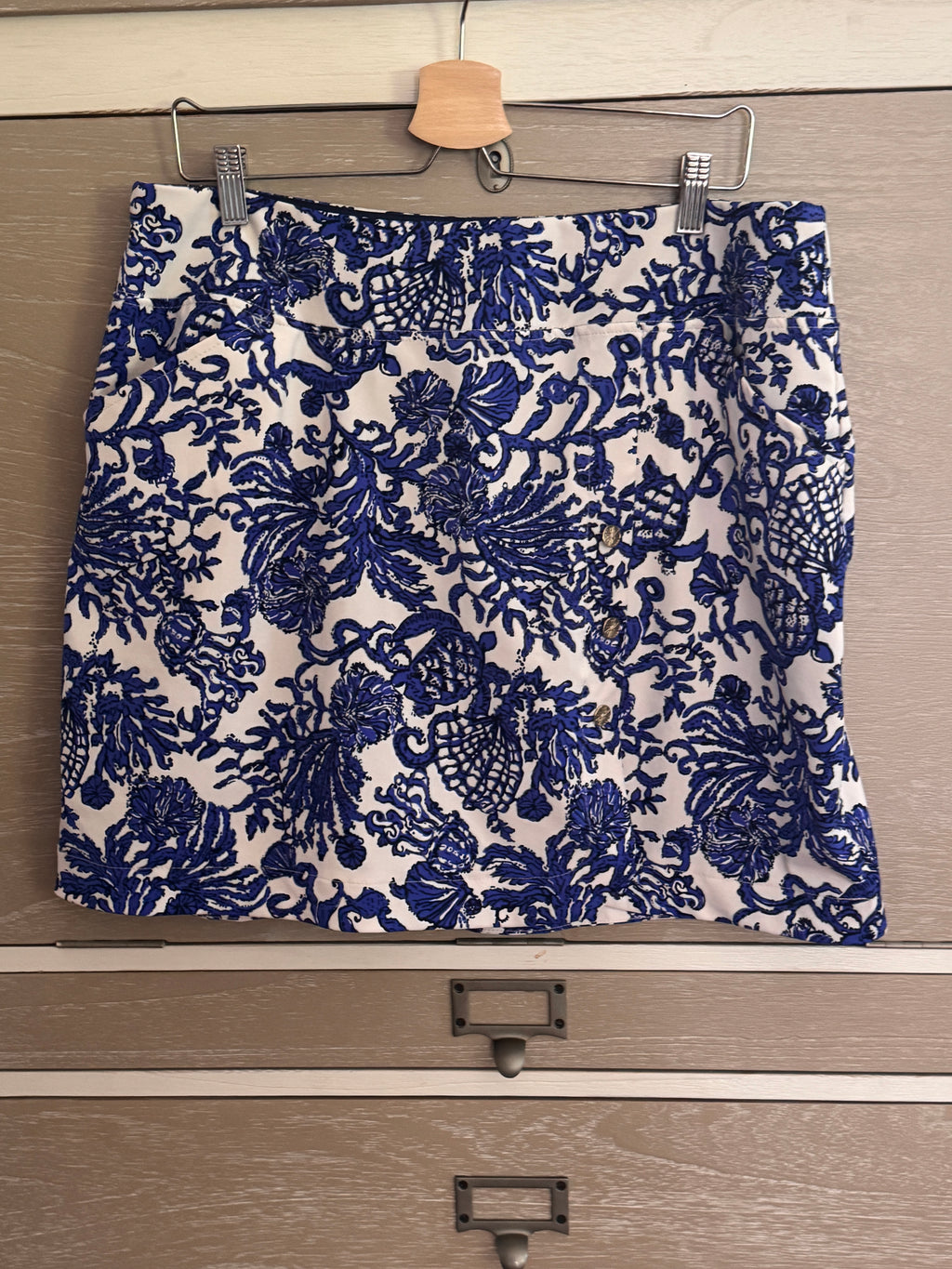A blue and white floral patterned skirt hanging from a wooden hanger on a metal clothes rail over a wooden drawer.
