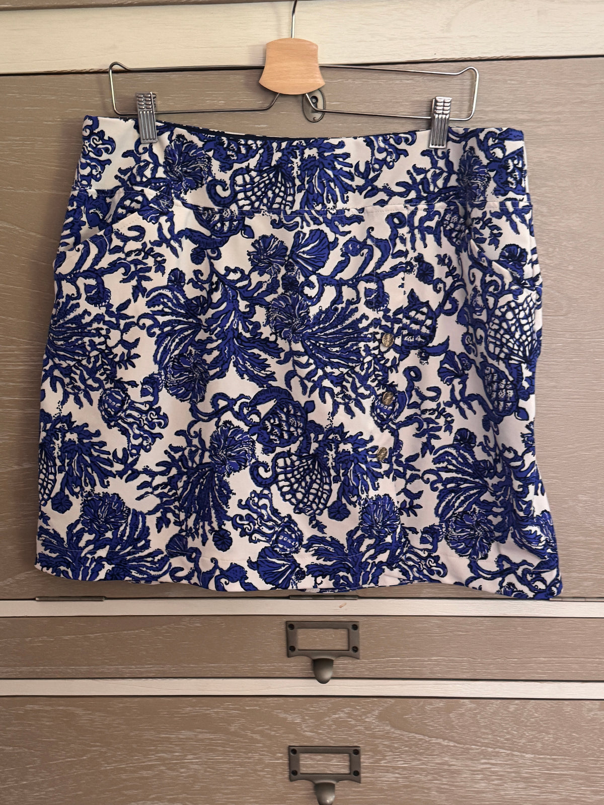 A blue and white floral patterned skirt hanging from a wooden hanger on a metal clothes rail over a wooden drawer.