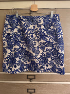 A blue and white jacquard patterned skirt hanging from a wooden hanger on a light wood drawer front.