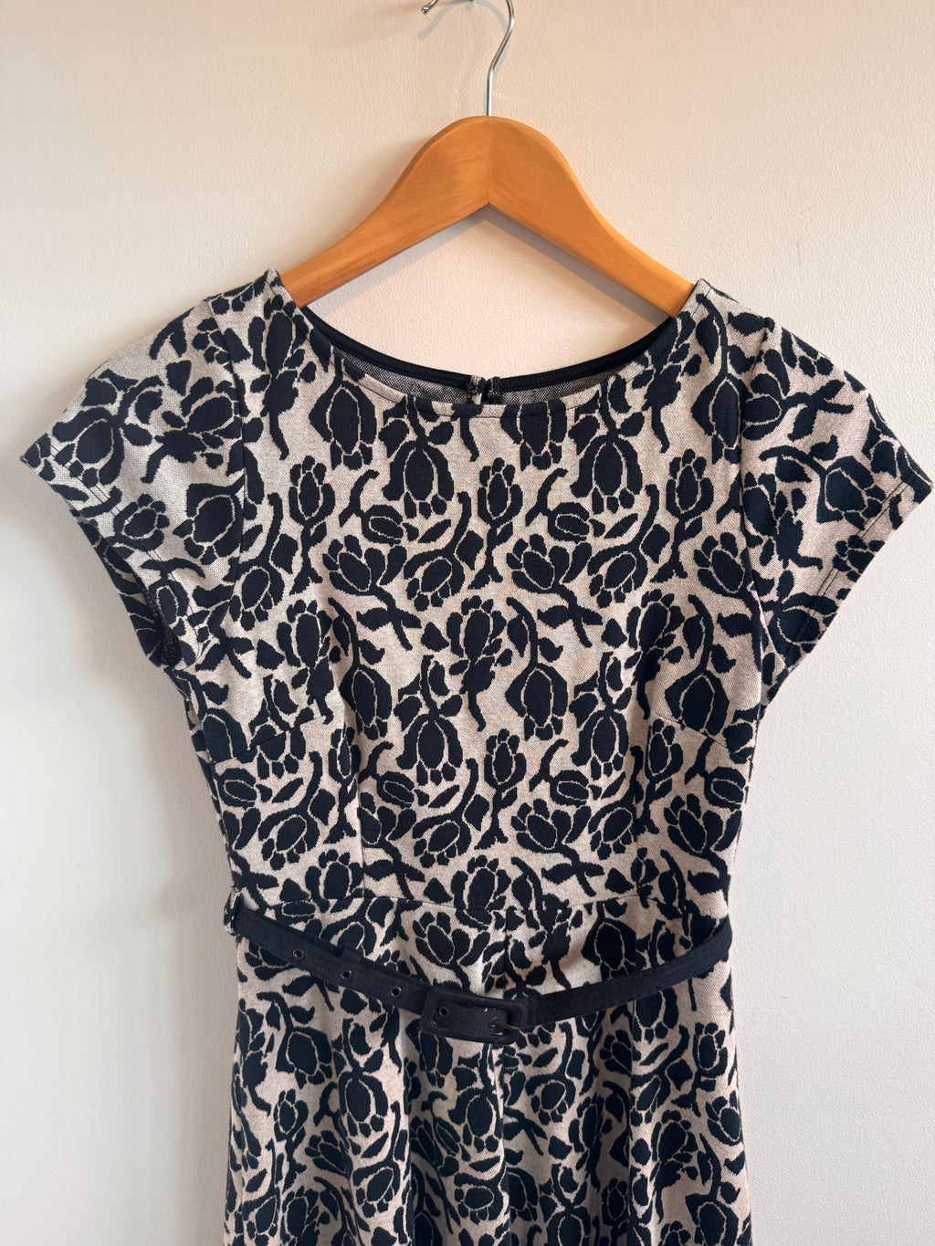 Black floral patterned dress on a wooden hanger against a white background