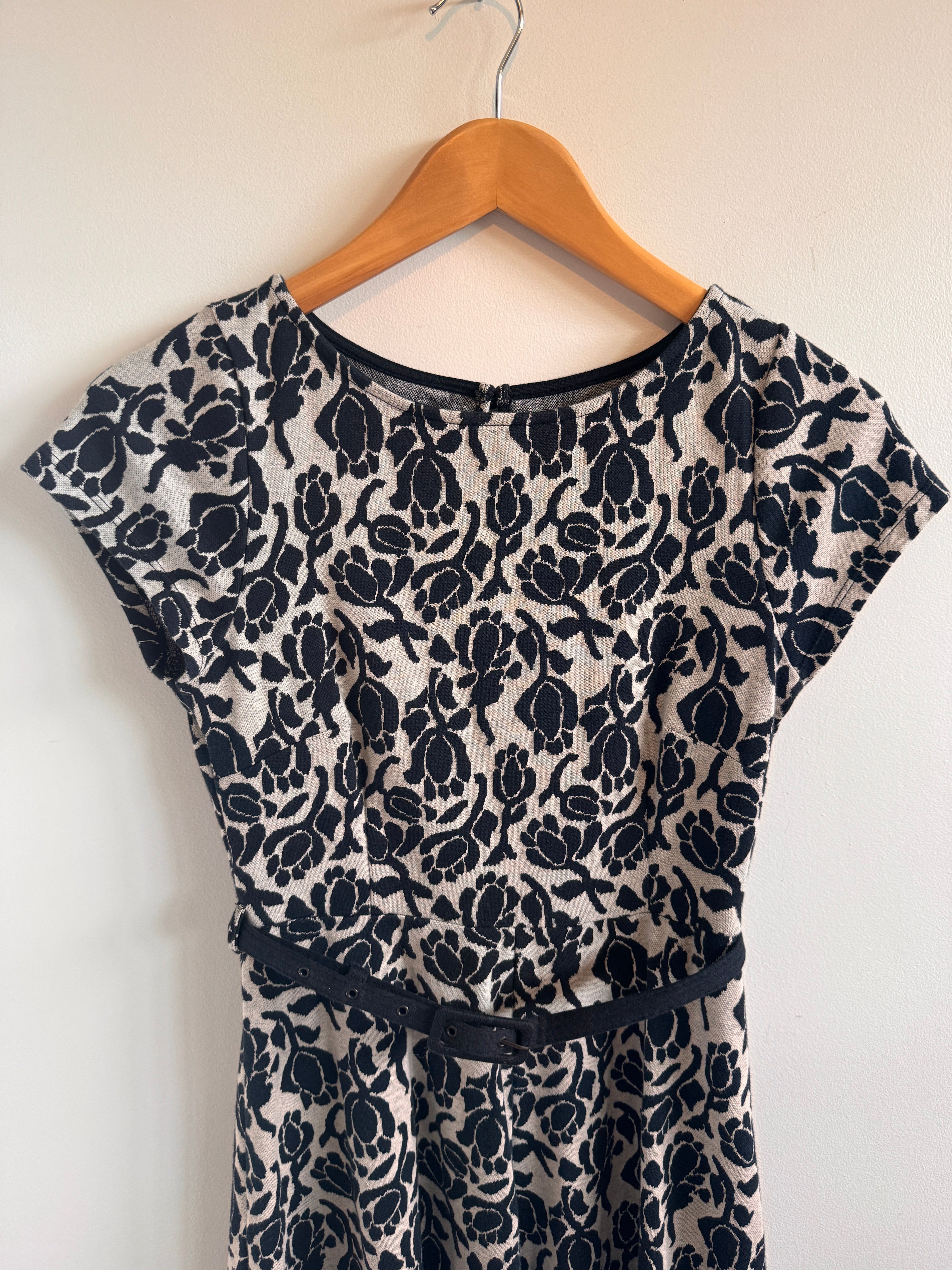 Black floral patterned dress on a wooden hanger against a white background