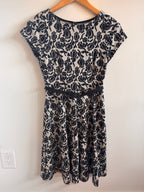 Black floral-patterned dress on a wooden hanger against a white wall.