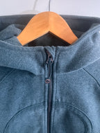 Close-up of a green denim jacket with a zipper on a wooden hanger against a light background