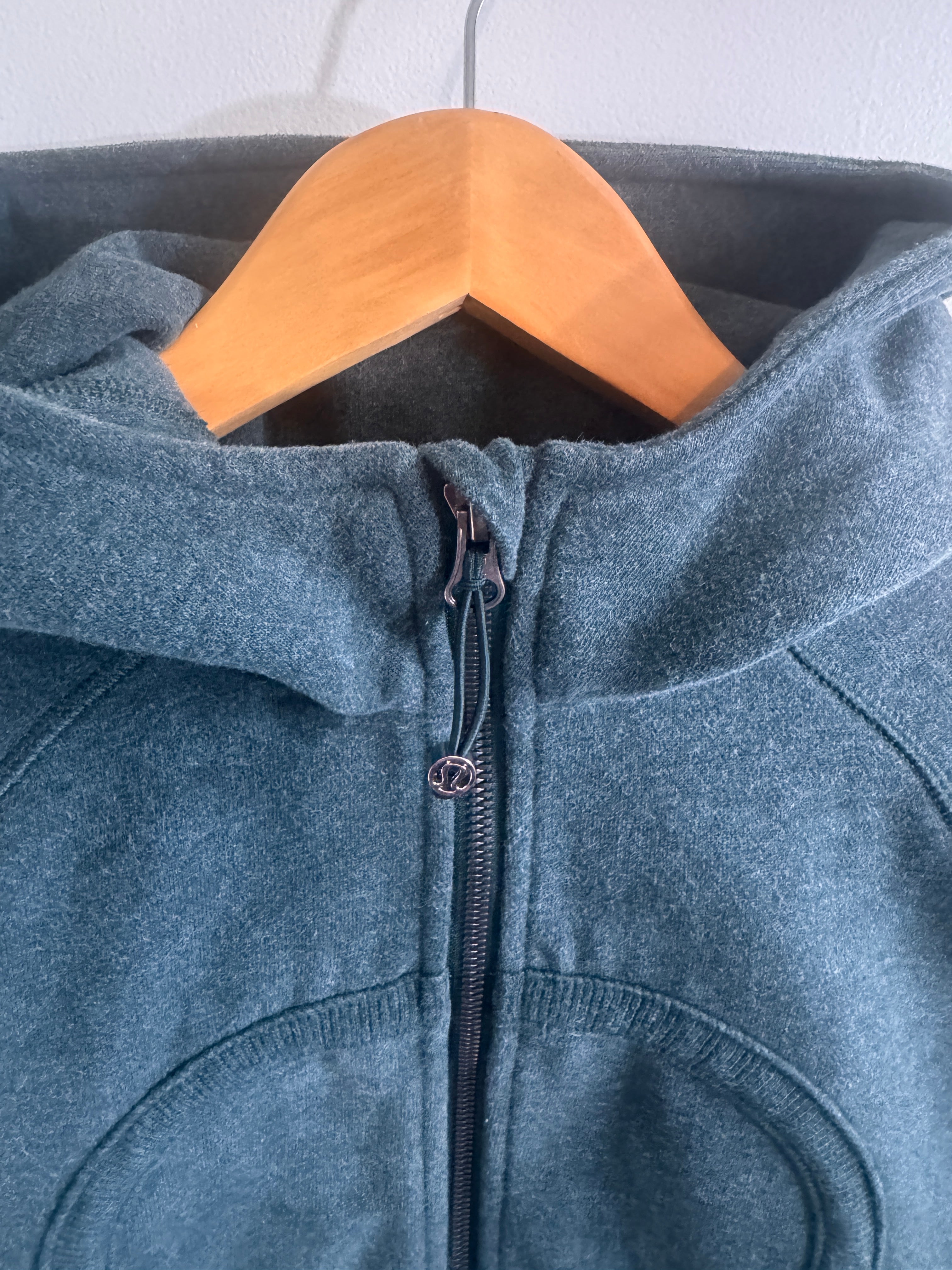 Close-up of a green denim jacket with a zipper on a wooden hanger against a light background