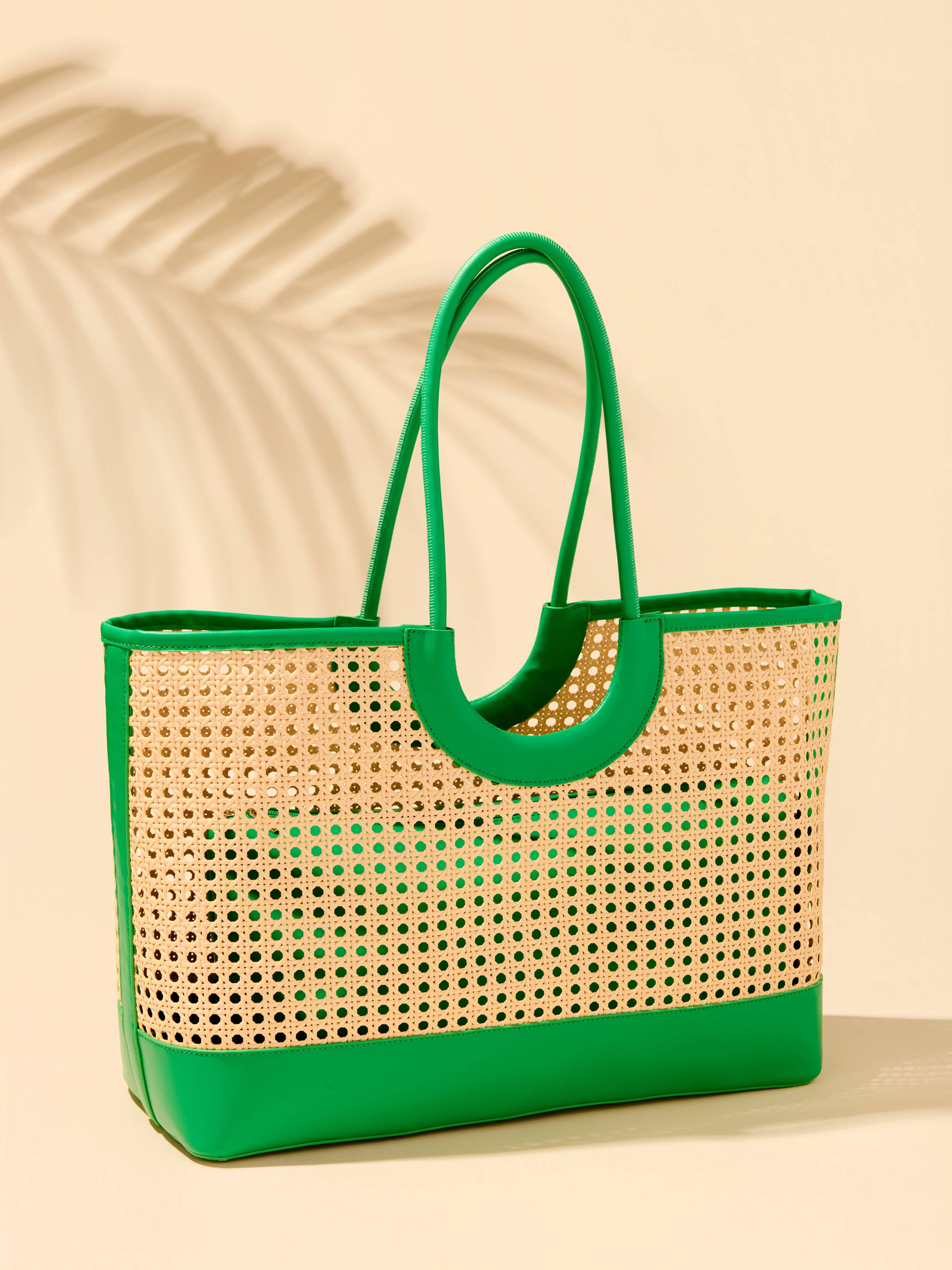 Woven tote bag with green handle and trim on a beige background