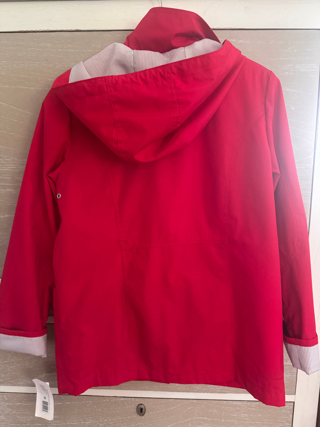 A bright red hooded rain jacket shown from the back, hanging on a light-colored wooden door. The interior hood lining and cuffs are light gray.