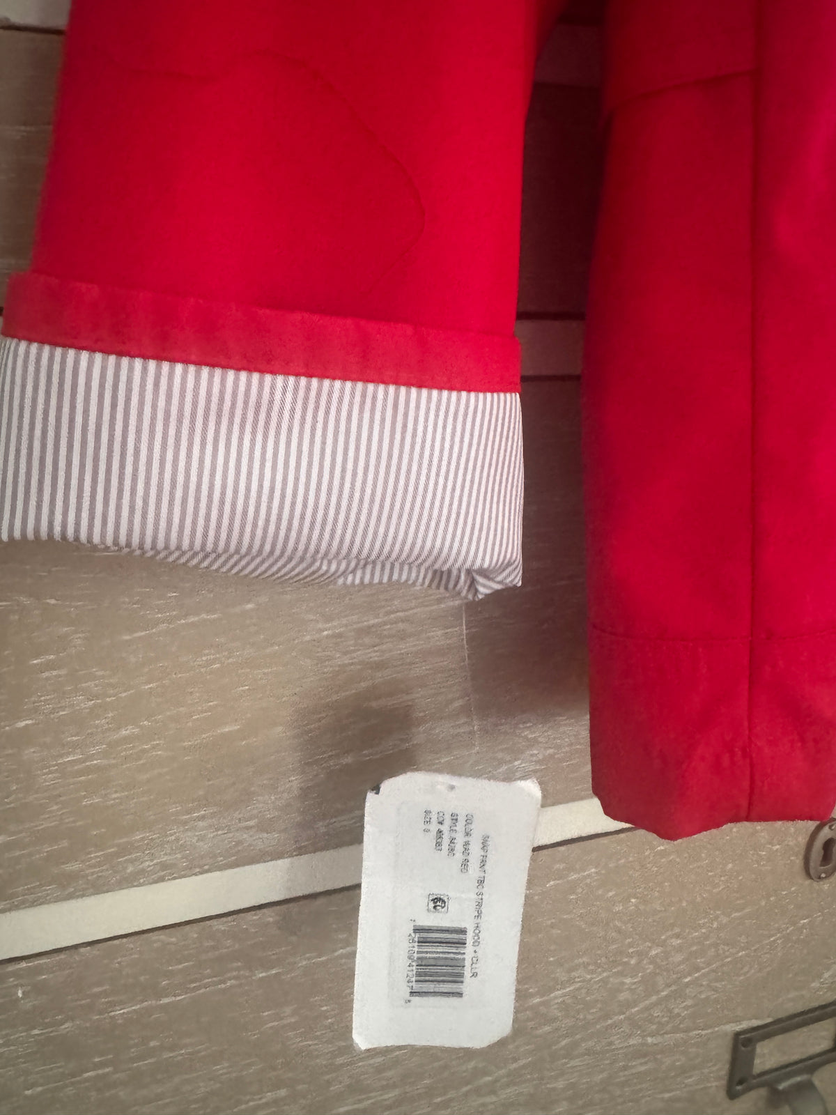 Close-up of a red garment, likely a jacket or coat, showing a striped lining cuff and a white product tag hanging below.